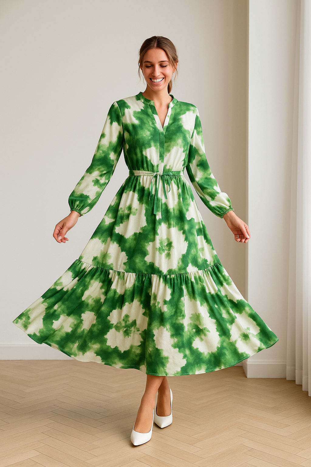 Vrouw in een elegante, lange maxi-jurk met groen-wit bloemenpatroon, gemaakt van luchtige stof. De jurk heeft lange mouwen, een strikceintuur in de taille en een vloeiende rok zonder naad onder de knie. Beschikbaar in maten S t/m 2XL.