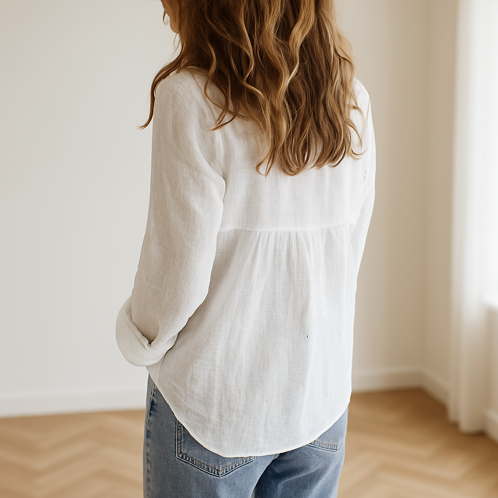 vrouw die een witte linnen damesblouse met lange mouwen draagt, staand in een lichte ruimte met natuurlijke lichtinval en een minimalistisch Zara-achtige achtergrond. De blouse heeft een luchtige pasvorm en is ideaal voor een zomerse, stijlvolle en duurzame outfit