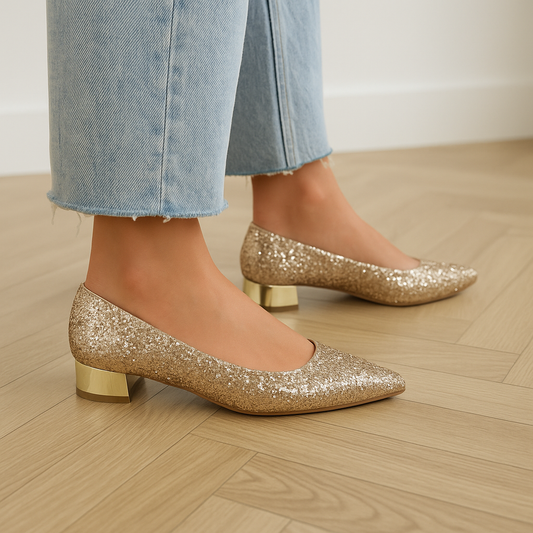 Goudkleurige glitterballerina's voor dames met een glimmende goudkleurige hak en spitse neus, gedragen met een denim jeans. Perfect voor feestelijke of chique gelegenheden.
